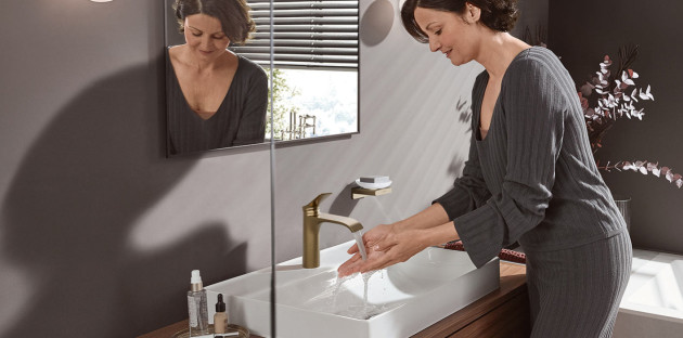 Femme utilisant un mitigeur de lavabo finition dorée dans une salle de bains contemporaine.