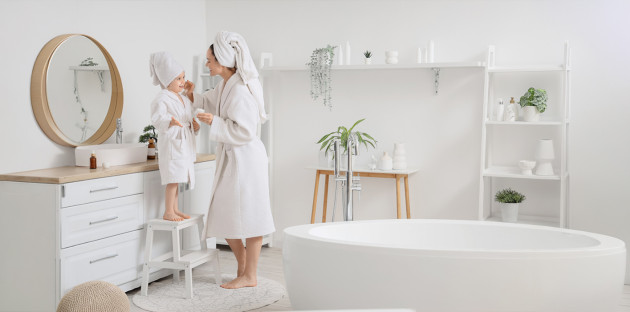 Mère et enfant en peignoir dans une salle de bains familiale lumineuse avec baignoire îlot et meuble vasque.