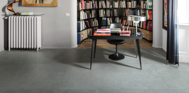 Sol en grès cérame gris grand format dans un bureau, ambiance contemporaine avec bibliothèque et radiateur design.