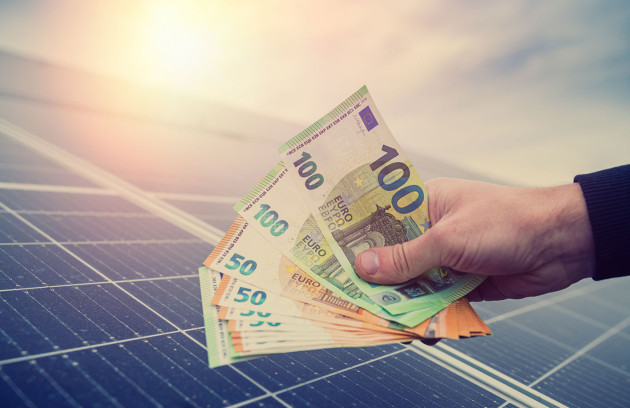 Personne qui tient des billets euro au dessus d'une installation de panneau solaire