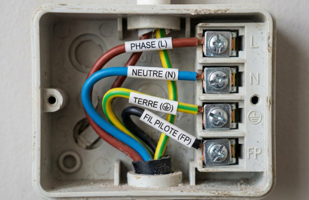 Bornier de raccordement d’un radiateur électrique avec fils identifiés phase, neutre, terre et fil pilote, illustrant le branchement conforme au circuit de chauffage.