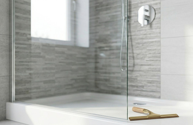 Paroi de douche vitrée propre avec raclette posée sur receveur dans une salle de bains moderne.