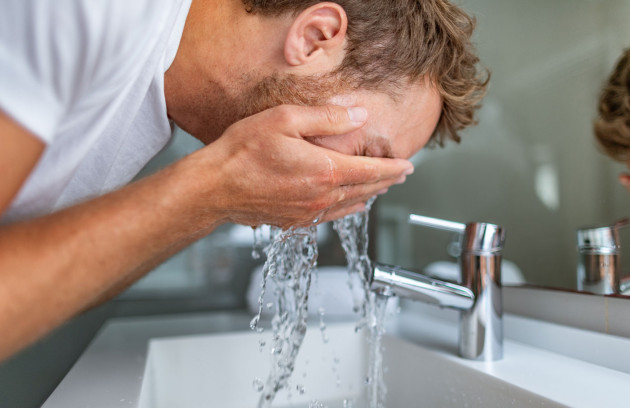 Homme utilisant un lavabo avec eau chaude sanitaire au robinet, illustrant l’usage domestique d’un chauffe-eau instantané pour un point de puisage en salle de bains.