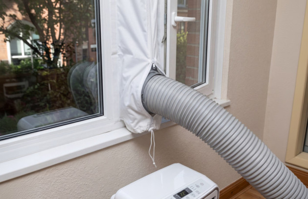 Mini climatiseur mobile installé près d’une fenêtre avec gaine d’évacuation et kit de calfeutrage pour rejeter l’air chaud vers l’extérieur