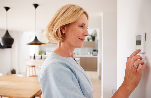 Femme réglant un thermostat mural digital pour optimiser la température et la consommation d’énergie de son chauffage.