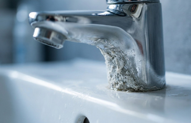 Robinet de salle de bains avec important dépôt de calcaire blanc à la base sur lavabo en céramique.