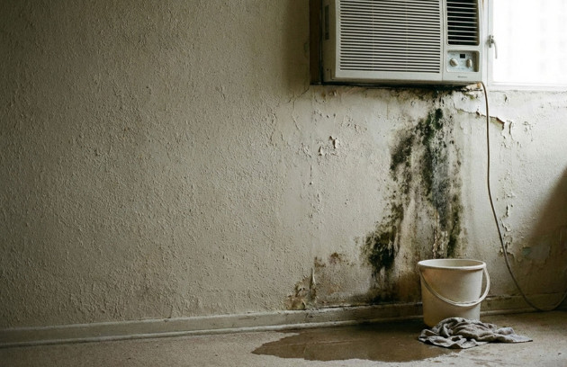 Climatiseur mural qui fuit avec écoulement d’eau de condensation, traces d’humidité et moisissures sur le mur, bac improvisé pour récupérer l’eau provenant d’un tuyau d’évacuation défectueux.