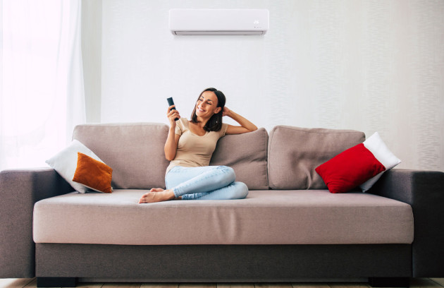 Climatisation murale réversible au-dessus d’un canapé, utilisation de la télécommande pour régler la température et profiter d’un confort thermique optimal sans surconsommation d’énergie.