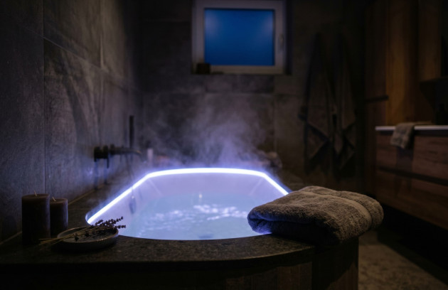 Baignoire balnéo éclairée en bleu dans une ambiance sombre propice à la détente.