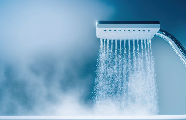 Pommeau de douche diffusant une eau chaude abondante avec vapeur, illustrant le débit et la température fournis par un chauffe-eau instantané pour la salle de bains.
