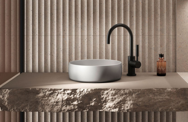 Vasque ronde blanche avec robinet noir, plan minéral et mur texturé.