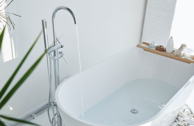 Remplissage d’une baignoire blanche avec robinet sur pied et douchette, salle de bains lumineuse.