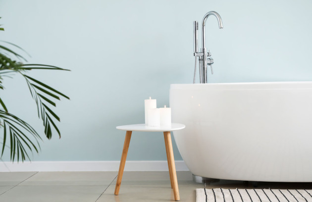 Détail d’une baignoire îlot blanche avec robinet sur pied, bougies et déco minimaliste.