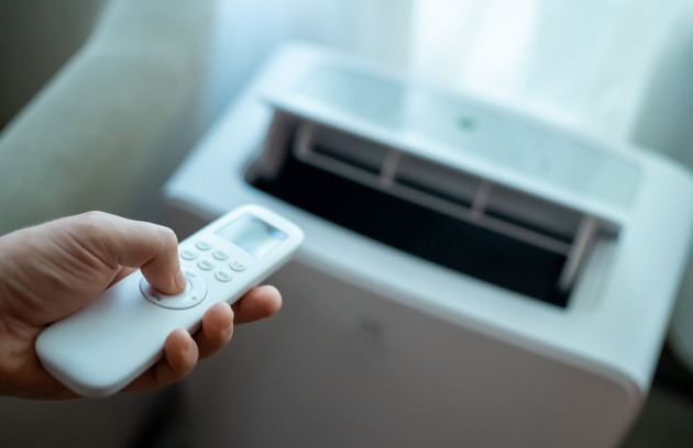 Télécommande réglant un climatiseur mobile, focus sur les boutons de commande et la sortie d’air.