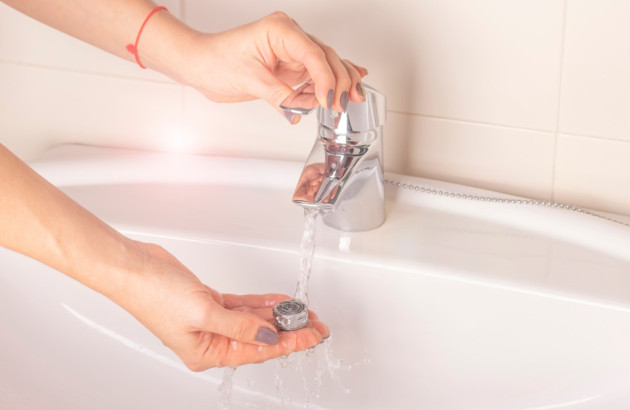 Nettoyage du mousseur de robinet sous l’eau dans un lavabo de salle de bains.