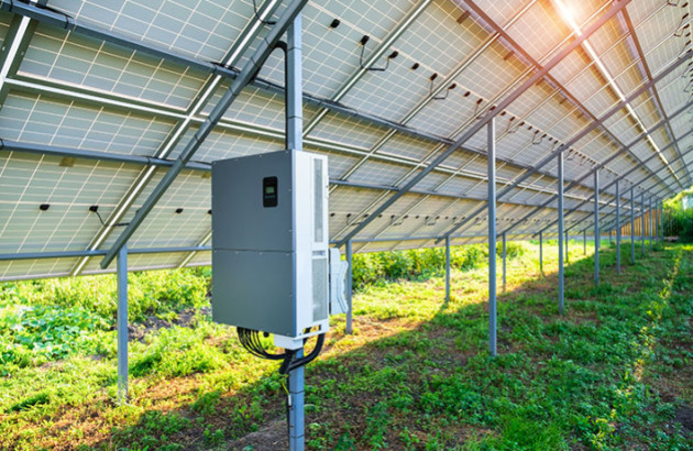 Onduleur solaire hybride posé sous une installation de panneaux solaires au sol