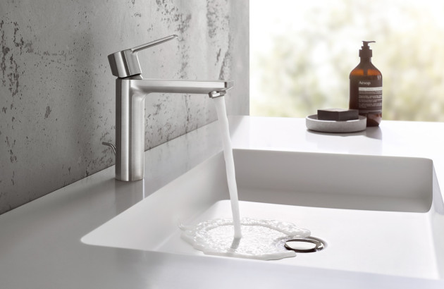 Mitigeur chromé faisant couler l’eau dans un lavabo blanc, salle de bains lumineuse.