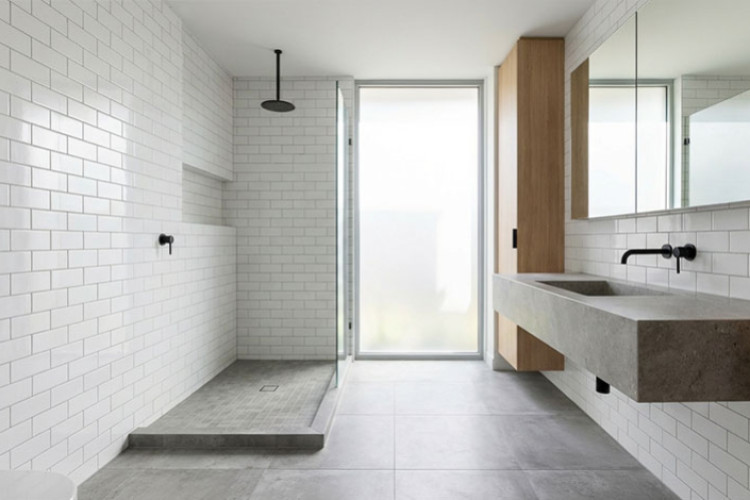 Salle de bains lumineuse avec faïence murale blanche type métro et carrelage gris au sol, douche à l’italienne et meuble vasque suspendu, illustrant le choix du carrelage et de la faïence.