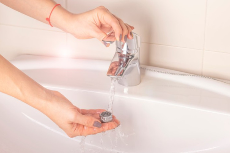 Nettoyage du mousseur de robinet sous l’eau dans un lavabo de salle de bains.