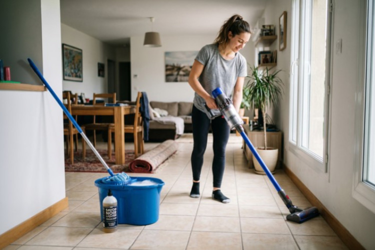 Personne nettoyant le carrelage d’un salon avec un aspirateur balai.
