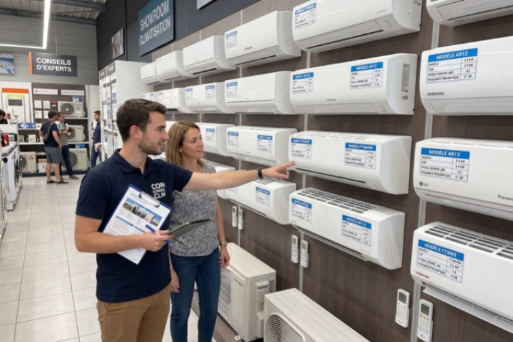 Conseiller en showroom présentant différents modèles de climatiseurs muraux pour aider au choix du système adapté.