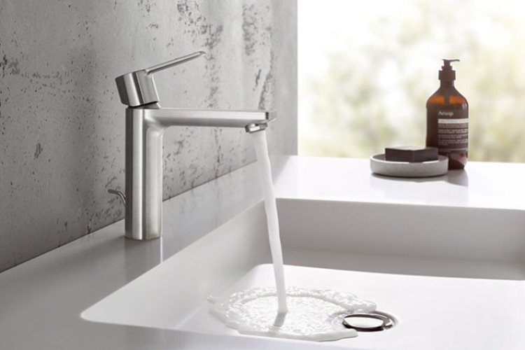 Mitigeur chromé faisant couler l’eau dans un lavabo blanc, salle de bains lumineuse.