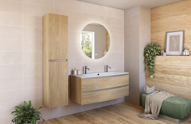 Meuble de salle de bain suspendu en bois clair avec double vasque, grand miroir rond rétroéclairé et colonne de rangement assortie sur carrelage beige.