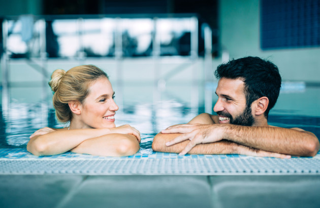 Couple souriant qui se regarde, s'appuyant sur le bord d'une piscine